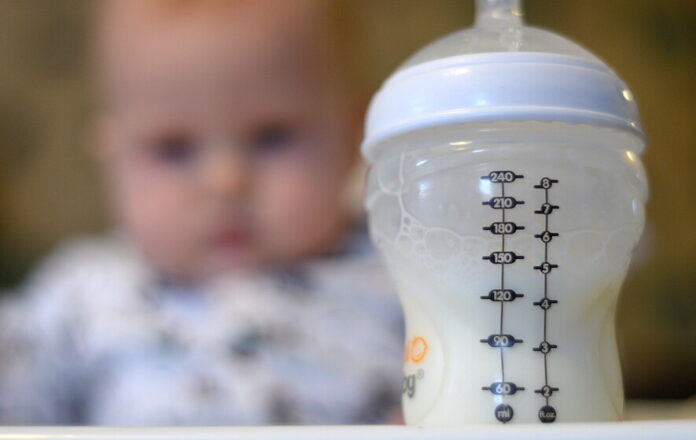 A baby in a high chair looks towards her bottle of milk in the foreground (PA)