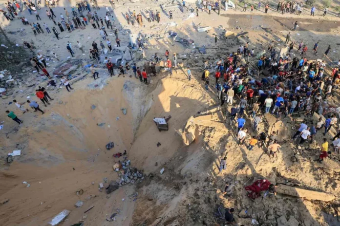Palestinians stand next to a crater caused by an explosion from an Israeli airstrike in Khan Yunis in southern Gaza on Oct. 16. MAHMUD HAMS/AFP VIA GETTY IMAGES