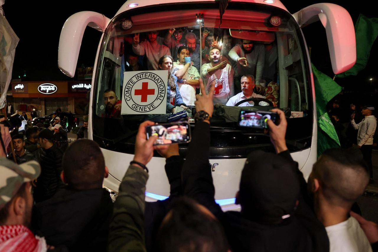A bus transporting Red Cross staff and Palestinians prisoners released from Israeli jails in exchange for hostages released by Hamas from the Gaza Strip drives through supporters holding flags in Ramallah in the occupied West Bank early on Nov. 26, 2023. AHMAD GHARABLI/AFP VIA GETTY IMAGES