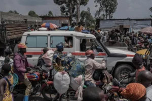 An ambulance drives on a road crowded with people fleeing the fighting in the Masisi territory. [Aubin Mukoni/AFP]