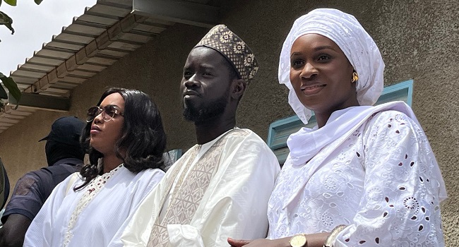 Presidential candidate for the Diomaye President coalition Bassirou Diomaye Faye (C), and his wives Marie Khone Faye (L) and Absa Faye (R) looks on after casting their ballots at the École Ndiandiaye polling station in Ndiaganiao on March 24, 2024 during Senegal’s presidential elections. (Photo by Khadidiatou Sene / AFP)
