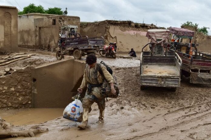 A man carries his belongings as he walks through a muddy street following a flash flood in Afghanistan's Baghlan province [AFP]