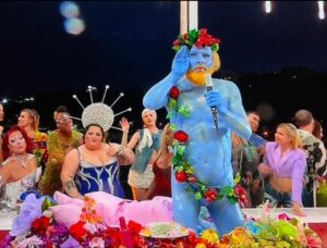 A performer painted blue and covered in flowers and fruit, depicting the Greek god Dionysus, sang in French