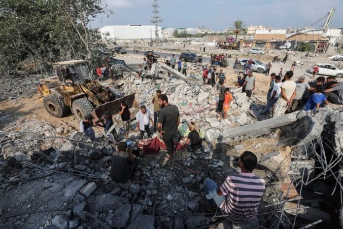 Palestinians stand at the site of an Israeli air strike on a shelter housing displaced people in central Gaza [Ramadan Abed/Reuters]