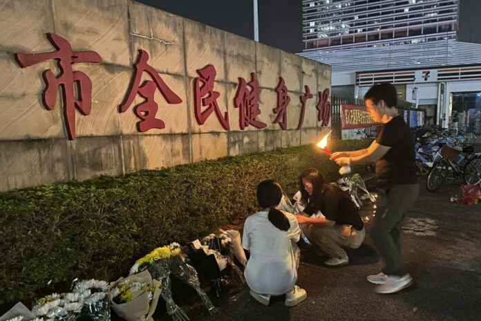 A woman lights a candle as offering near flowers placed outside the 