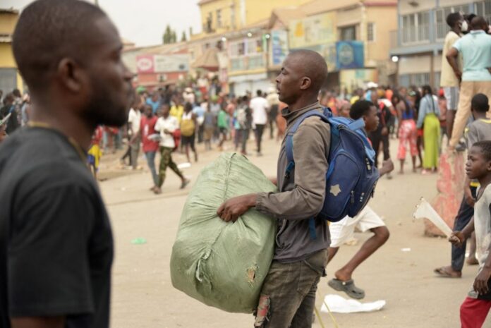 A man carries a bundle of goods as looting erupted in the Kalemba 2 district of Luanda on July 28, 2025, during a general strike in the taxi sector declared for three days to protest against the rising prices of fuel. The looting happened after some 2,000 people protested on Saturday in Luanda, the capital of Angola, to denounce the rise in fuel prices and transportation costs, waving placards hostile to the government, an AFP correspondent observed. A significant deployment of police in riot gear supervised the protest, organised at the call of several civil society associations. Previous demonstrations had taken place on Saturdays, July 12 and 19. (Photo by AFP)
