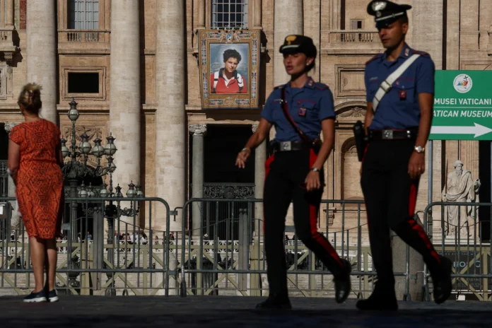 Carabinieri walk past a tapestry hanging from the facade of St. Peter's Basilica at the Vatican depicting an image of Carlo Acutis, a British-born Italian boy who will become the first millennial to be made a Catholic saint in a ceremony led by Pope Leo, as seen from Rome, Italy, September 4, 2025. REUTERS/Guglielmo Mangiapane