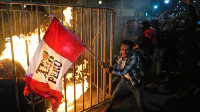 A demonstrator waves a Peruvian flag as a cardboard doll burns in front of Congress in Lima, Peru, on October 15, 2025.