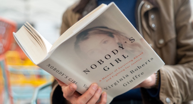 A person poses for a photo with a copy of the book “Nobody’s Girl – A Memoir of Surviving Abuse and Fighting for Justice” by Virginia Roberts Giuffre, in central London on October 21, 2025, on the day of its release in the UK. Photo by NIKLAS HALLE’N / AFP