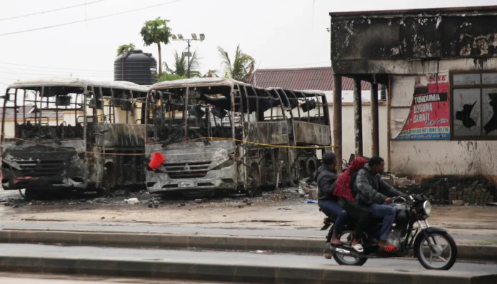 People ride a motorcycle past the wreckage of buses burnt during protests, following a general election marred by violent demonstrations over the exclusion of two leading opposition candidates, at the Mwembechai area in Kinondoni district in Dar es Salaam, Tanzania, November 4, 2025. REUTERS/Emmanuel Herman
