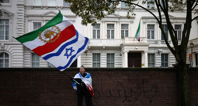 An anti-Iranian regime protester waves the Iranian flag before the 1979 revolution with the Lion and Sun emblems with an Israeli flag outside the Iranian Embassy, central London, on January 9, 2026. Iran FM says US, Israel ‘directly intervening’ in protests. Iran’s foreign minister accused the United States and Israel on Friday of fuelling a growing protest movement in the country, while dismissing the possibility of direct foreign military intervention after US warnings over crackdowns on demonstrators.