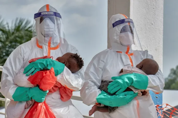 Congolese medical workers dressed in personal protective equipment carry children tested and cleared of Ebola virus infections at a secured Ebola response zone in Bunia town, Ituri province [File: Gradel Muyisa Mumbere/Reuters]